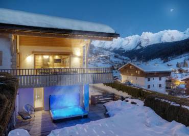 Vue extérieure du chalet la nuit, avec jacuzzi et vue sur les montagnes